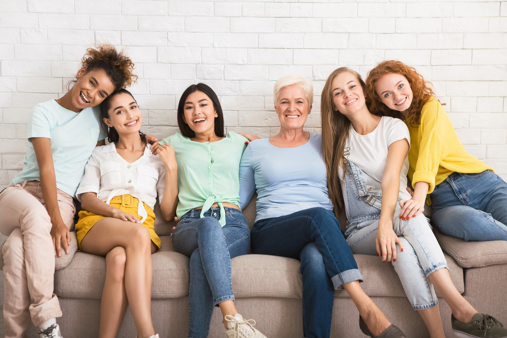 Diverse Women Hugging Sitting On Couch Against White Wall Indoor
