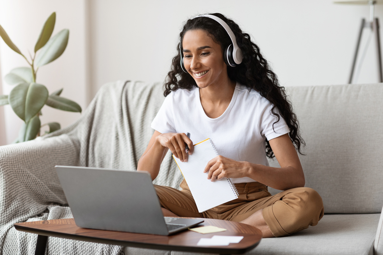 Cheerful lady attending online course, using laptop and wireless headset